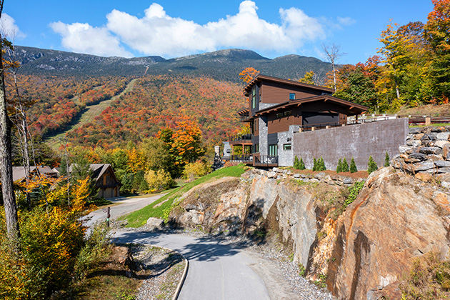 Mountain lodge overlooking a scenic landscape of autumn foliage, with vibrant trees covering the hills and a clear blue sky above.