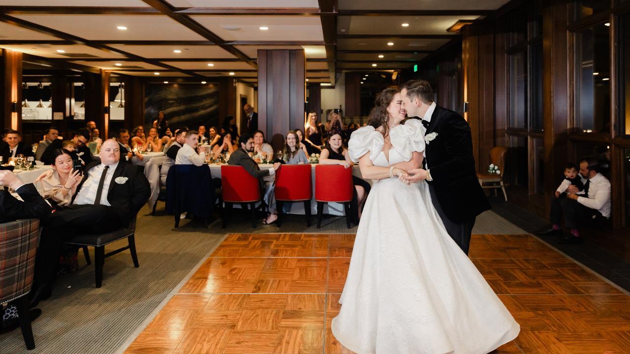 Bride and groom enjoying their first dance in a beautifully decorated reception hall, surrounded by guests seated at elegantly set tables.