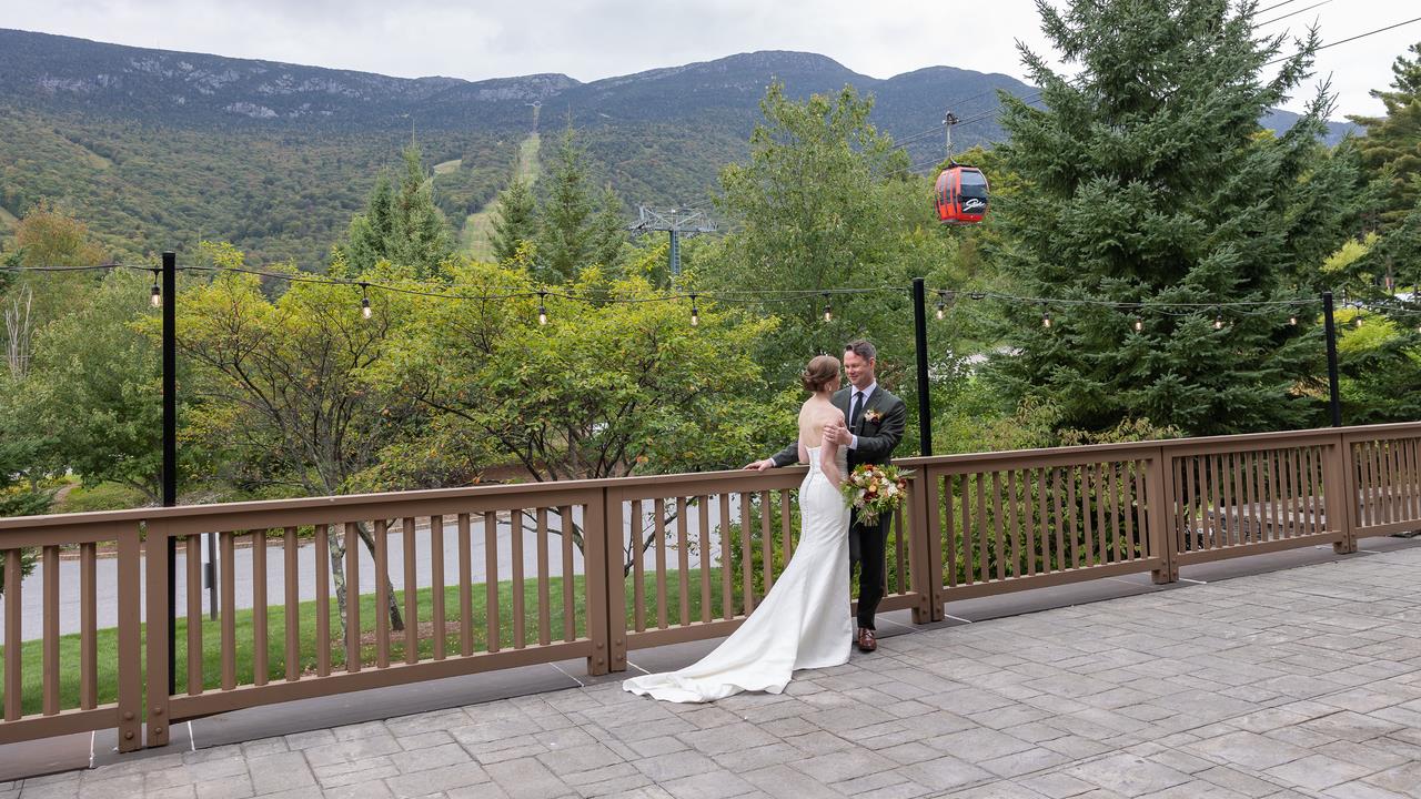 Bride and groom sharing a quiet moment on an outdoor patio with lush greenery, mountains, and a cable car in the background.